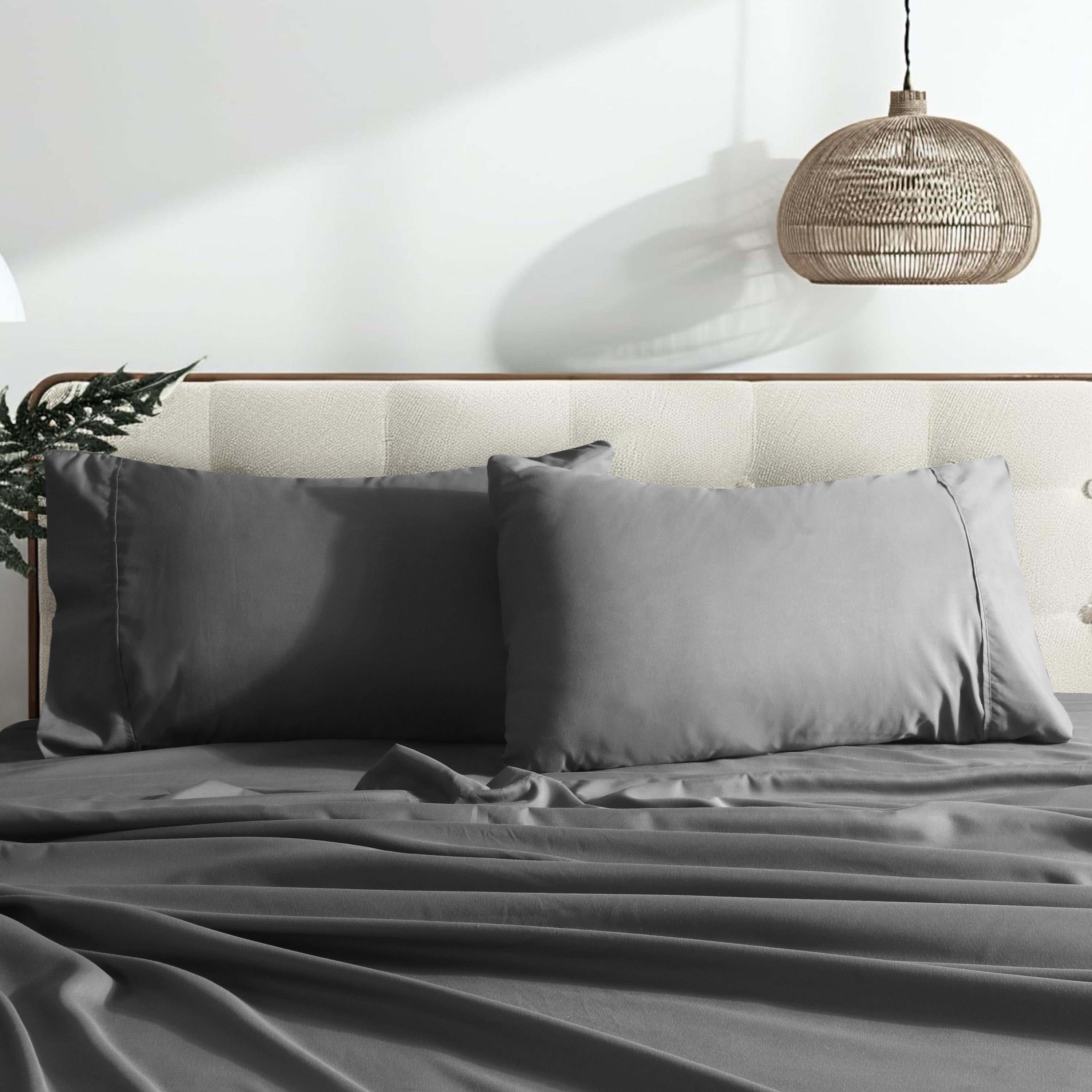 Gray bedding set on a bed with a neutral headboard and hanging light fixture.